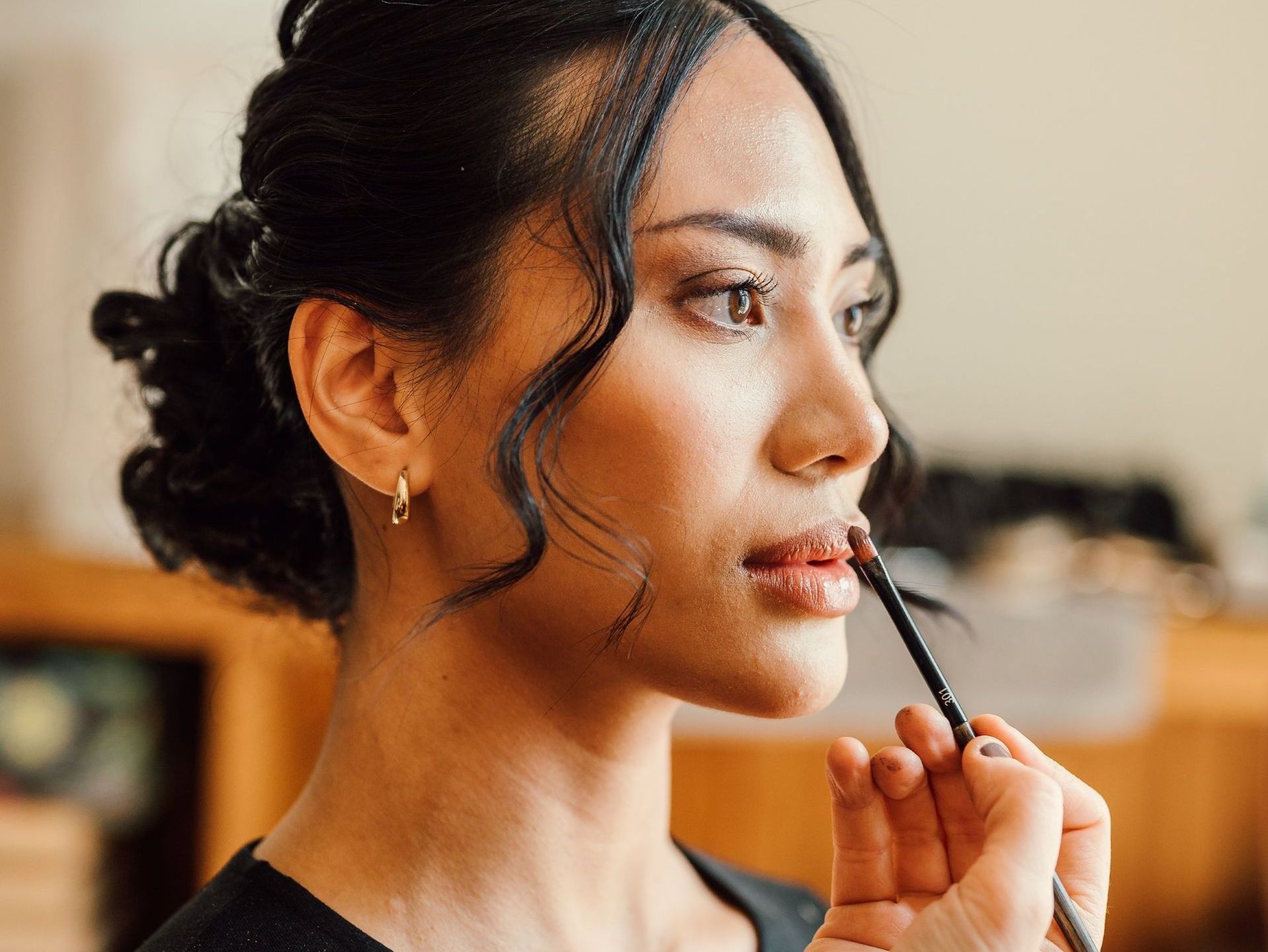 Kvinna med uppsatt hår och makeup får läppglans applicerat.